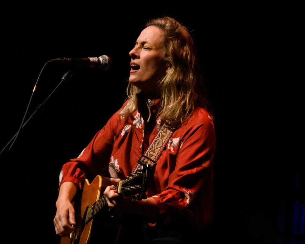 Sarah Harmer sings into a microphone while playing acoustic guitar during a performance at the Kingston Grand Theatre, May 2022