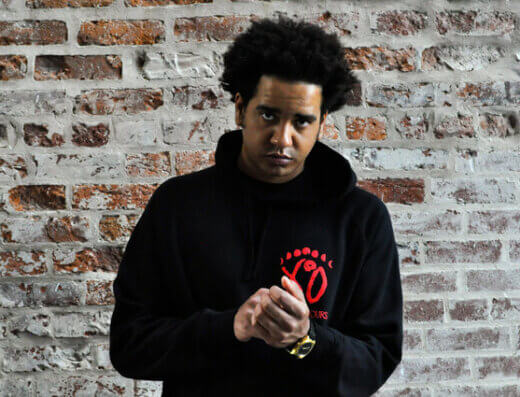 Kingston hip hop artist, Keaton, poses against a brick wall.