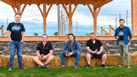 The Kingston Live podcast crew poses with Dan MacKinnon and Ben Vandenberg of MacKinnon Brothers Brewing Co. with bales of hay.
